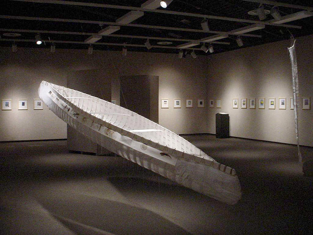 A canoe made of paper is on display in a dark exhibition room. 