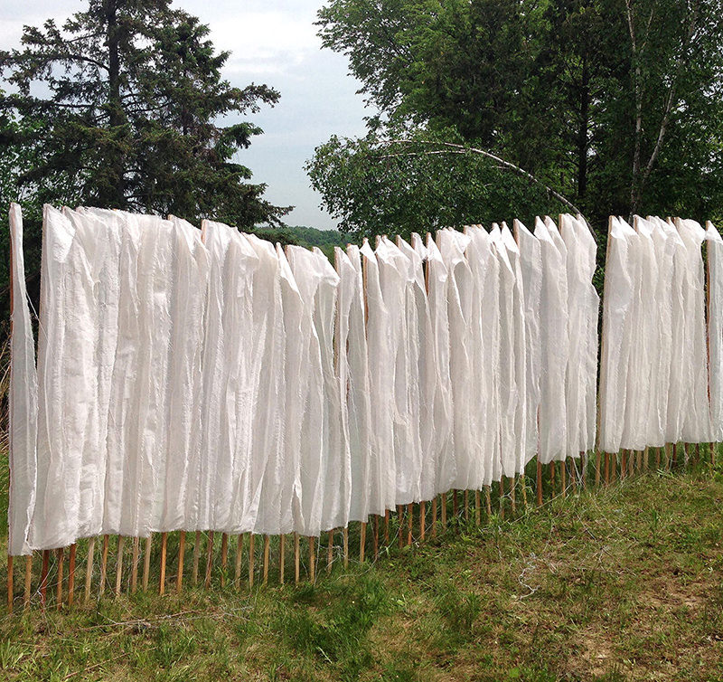 Pieces of white cotton are attached to wooden stakes planted into the ground in nature. 