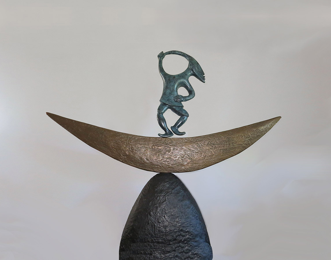 A bronze sculpture of a figurine dancing on a stylized moon crescent. 