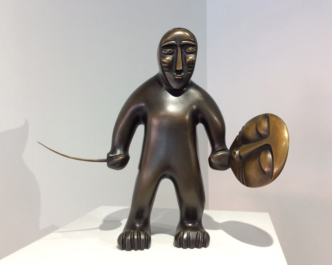 A bronze sculpture of a figurine holding a drum and a drumstick. 
