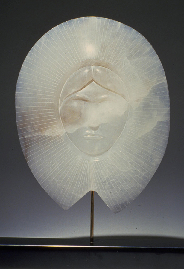 An alabaster sculpture of a woman’s face crowned by sunrays. 