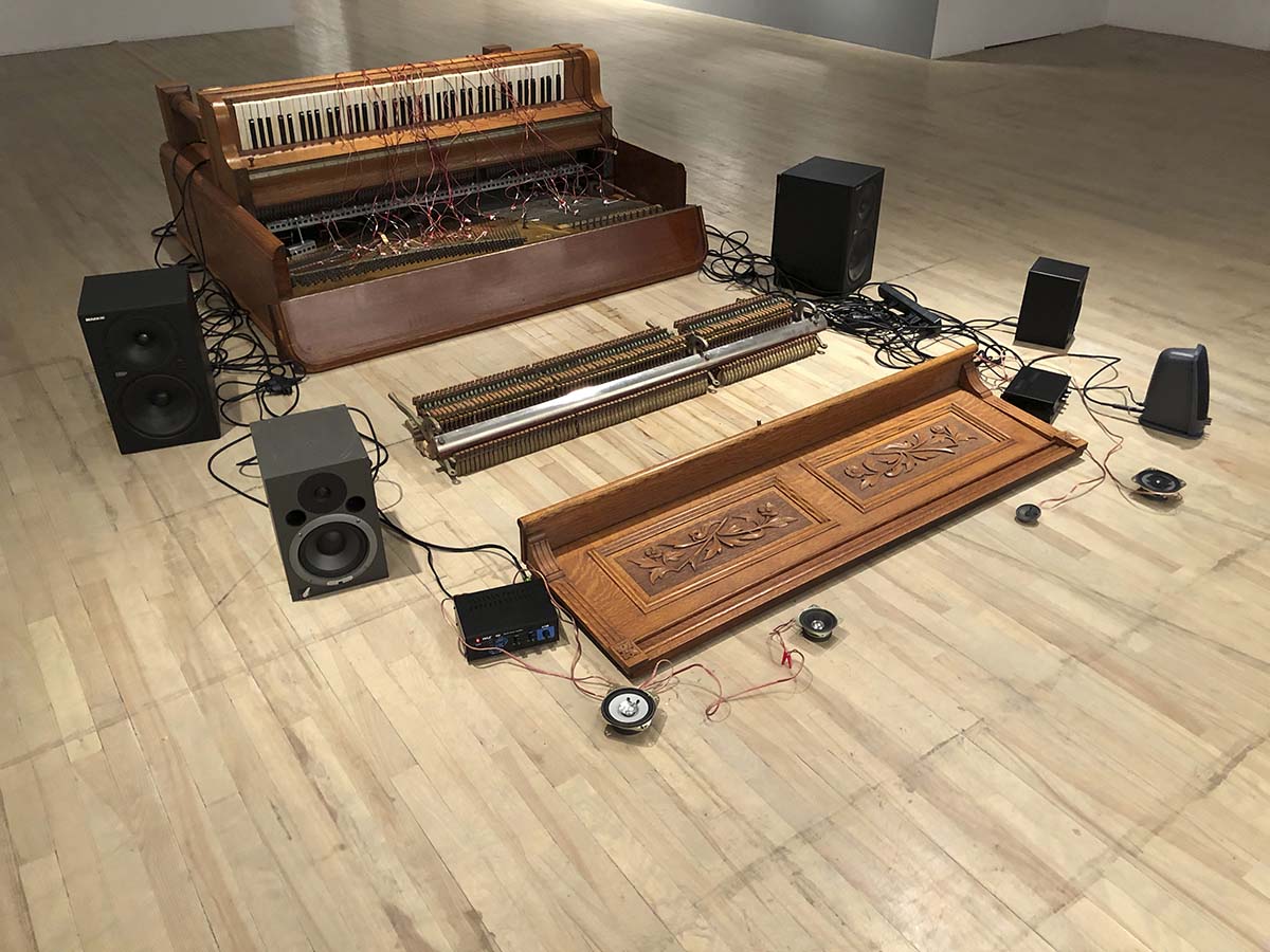 An installation showing a deconstructed piano and a sound system on the floor of an exhibition hall. 