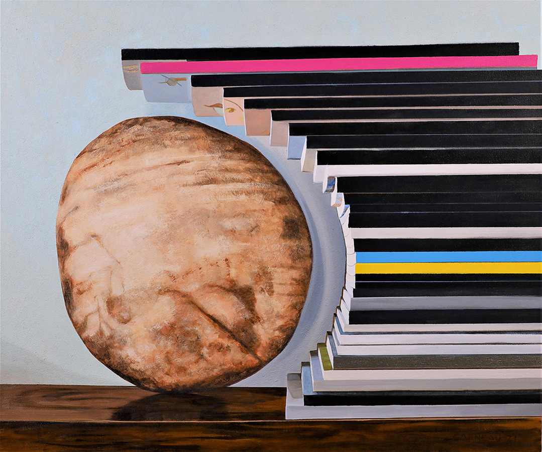 The edge of a horizontal stack of thin, paper-bound books conforms to the contour of a rounded rock sitting on a table. 