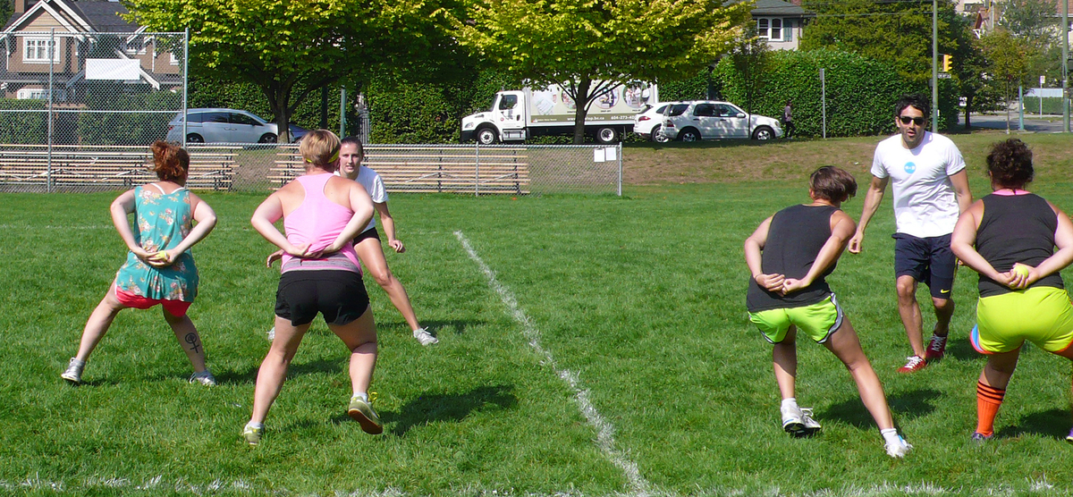 Six people in athletic clothing are shown playing on a sports field. Some have both hands behind their backs, holding tennis balls. 