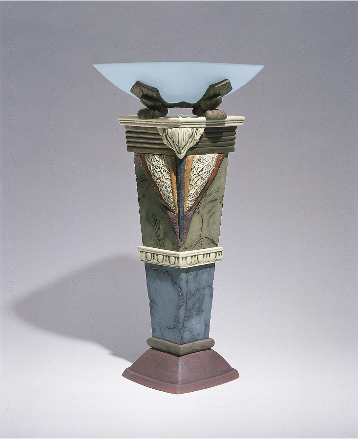 A flared, translucent glass bowl, supported by a four-sided ceramic column, glazed in muted green, blue and red. 