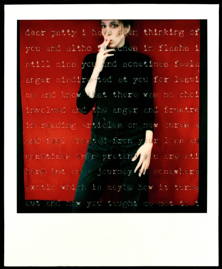 A person dressed in black standing against a red background smoking a cigarette with superimposed lettering.  
