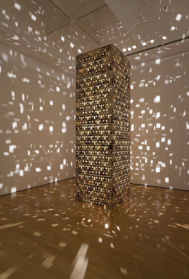A light-filled cardboard tower casting shapes on surrounding walls. 