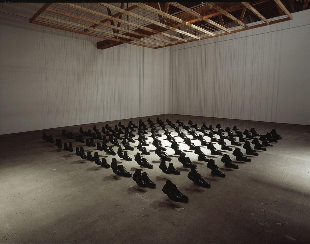 Many pair of combat boots suspended under a spotlight.  