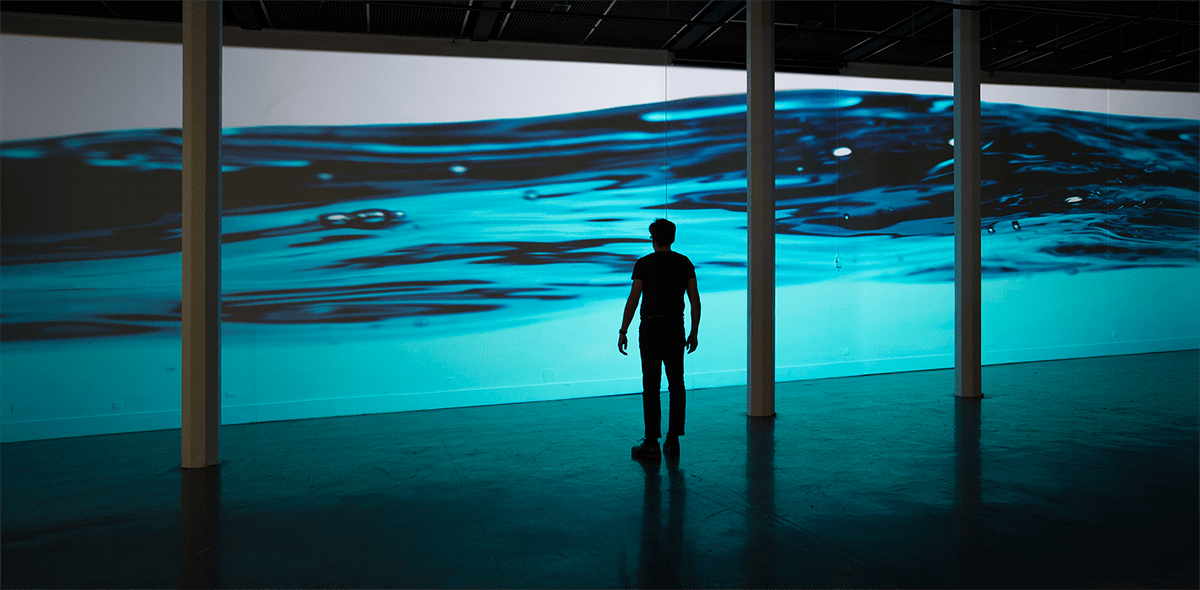 A photo of a man standing before a large projected image of blue water. 
