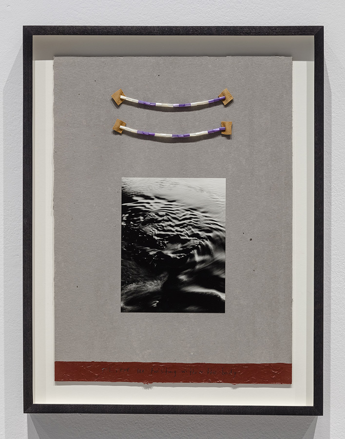 A black-and-white photo of water under two pieces of wampum inside a black frame.  