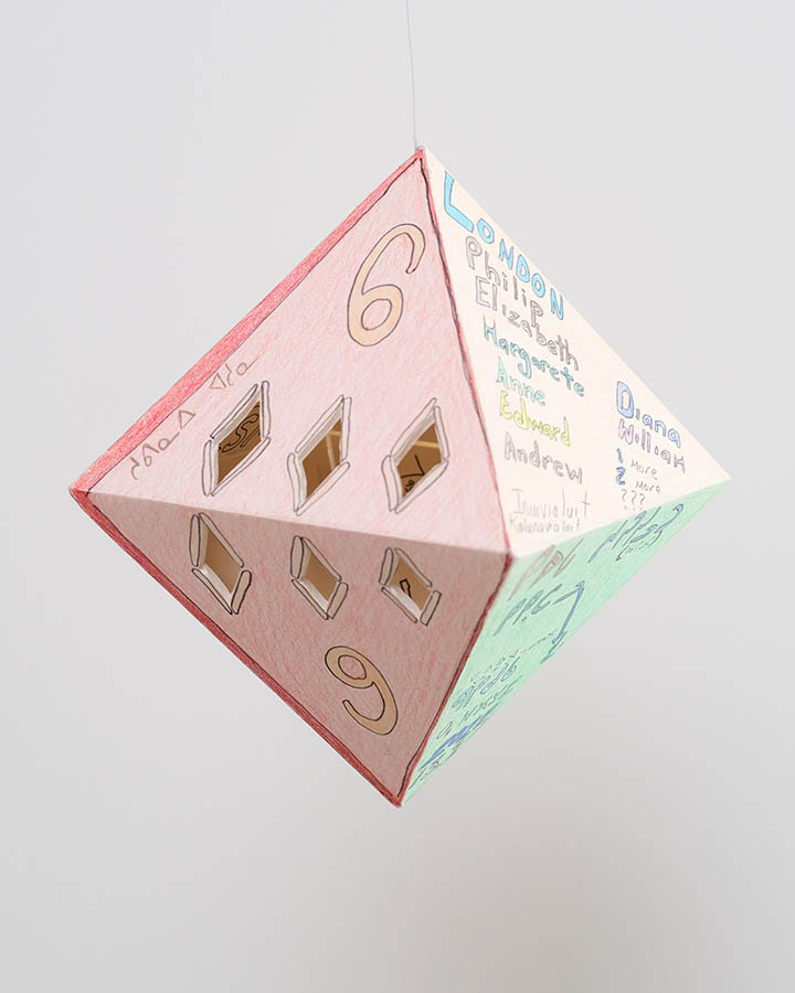 Drawings and words written around cut-outs on all sides of a prism. 